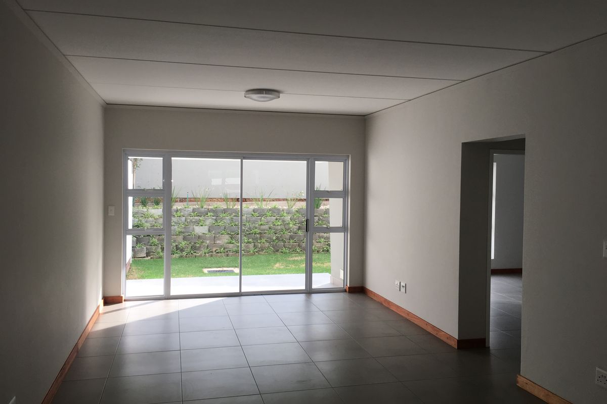 A bright, empty living room featuring neutral tiled floors, modern skirting boards, and a large sliding glass door providing access to the rear garden.