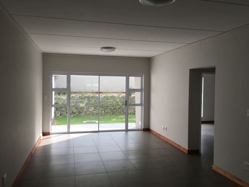A bright, empty living room featuring neutral tiled floors, modern skirting boards, and a large sliding glass door providing access to the rear garden.