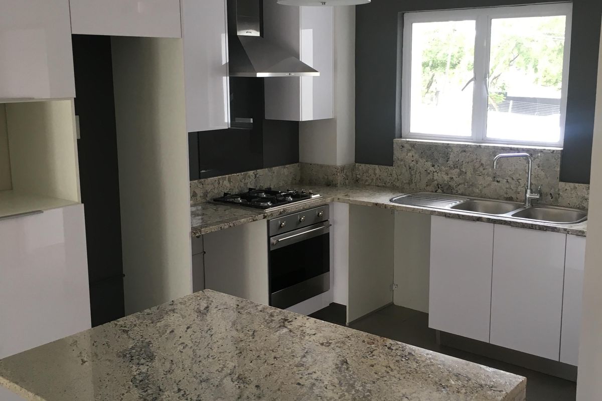 Modern kitchen featuring gloss white cabinetry, granite countertops, a central island, and built-in stainless steel appliances.