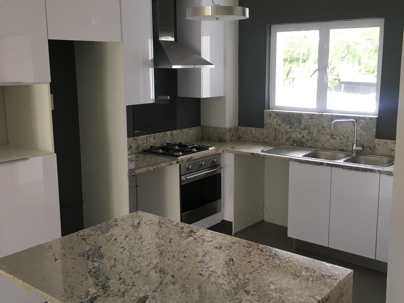 Modern kitchen featuring gloss white cabinetry, granite countertops, a central island, and built-in stainless steel appliances.