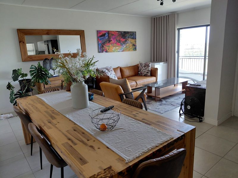 An open-plan living and dining area featuring tiled flooring and a large sliding glass door leading to a balcony.