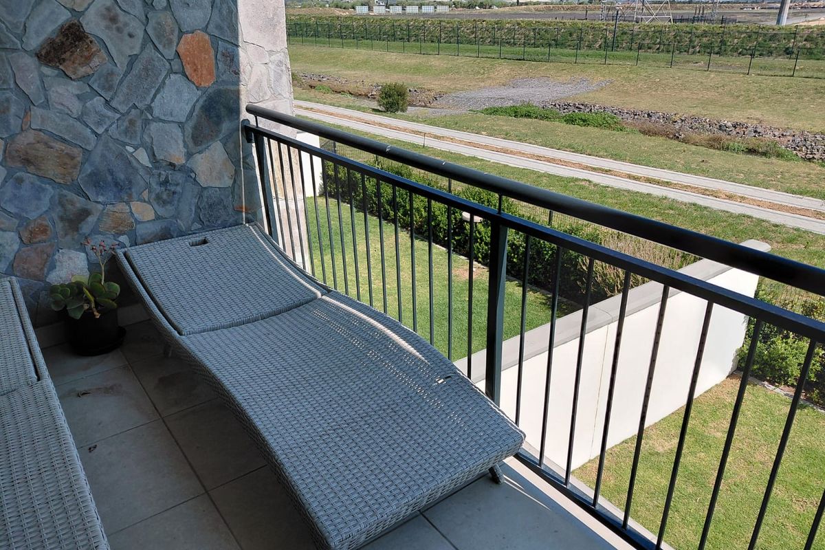 A private balcony featuring stone wall cladding, tiled flooring, and a metal balustrade overlooking a landscaped green area.