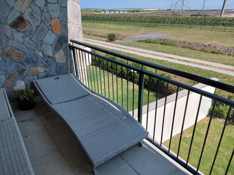 A private balcony featuring stone wall cladding, tiled flooring, and a metal balustrade overlooking a landscaped green area.