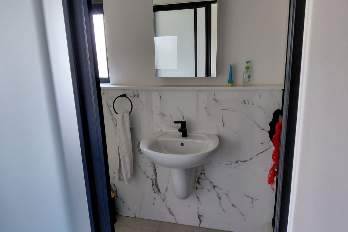 A modern bathroom featuring a pedestal basin with a black mixer tap, complemented by elegant marble-look wall tiling and a wall-mounted mirror.