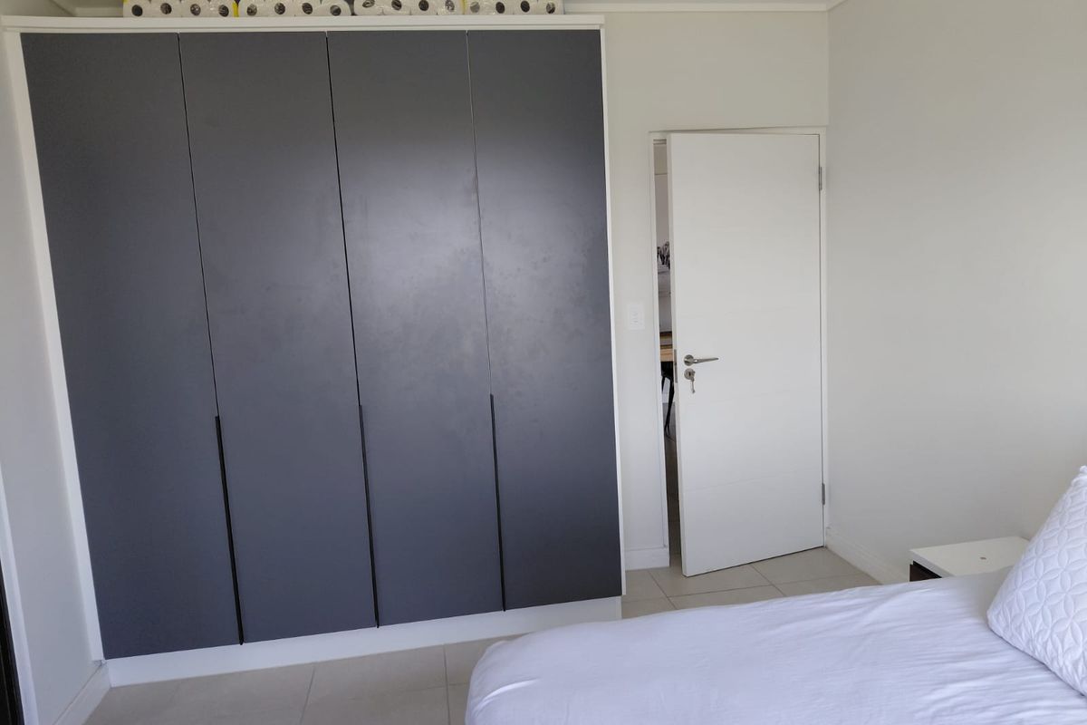 A bedroom featuring a modern dark grey built-in wardrobe, tiled flooring, and a white internal door leading to an adjacent room.
