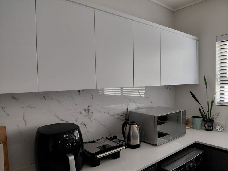 Modern kitchen featuring sleek white cabinetry, a marble-effect splashback, and clean stone countertops with integrated window blinds.