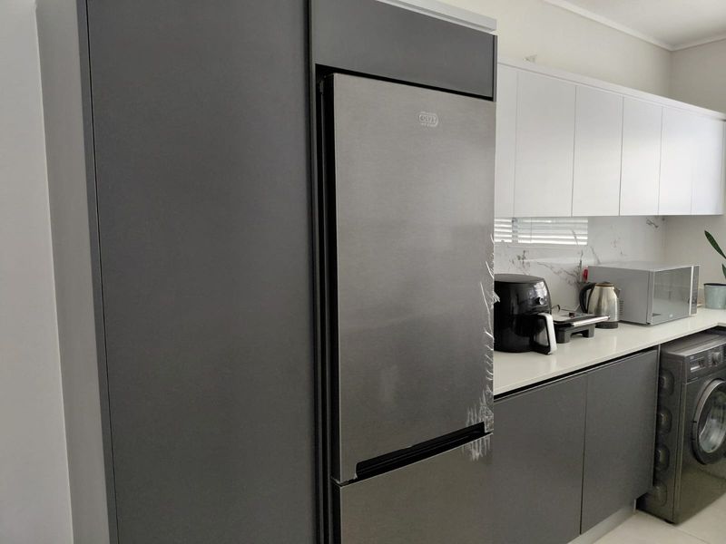 Modern kitchen featuring sleek dark grey cabinetry, white upper cabinets, stone countertops, marble-look splashback, and integrated appliances.