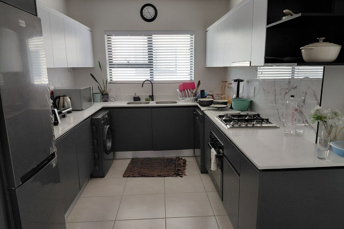 Modern galley-style kitchen featuring sleek grey cabinetry, white stone countertops, integrated gas hob, built-in oven, and tiled flooring with ample natural light.