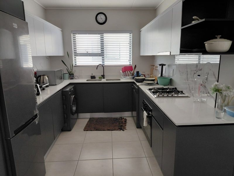 Modern galley-style kitchen featuring sleek grey cabinetry, white stone countertops, integrated gas hob, built-in oven, and tiled flooring with ample natural light.