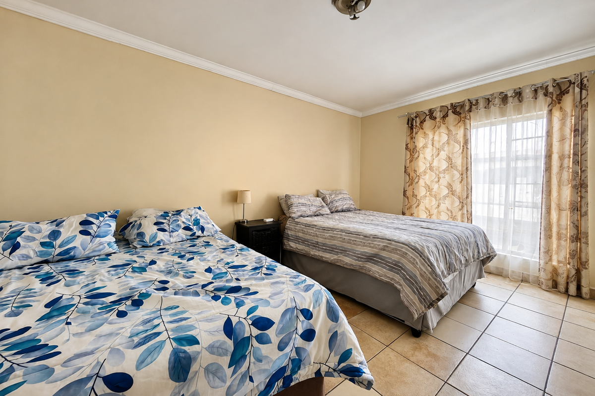 A spacious bedroom featuring neutral wall tones, tiled flooring, and a large window with curtain treatments, providing a functional and comfortable living space.