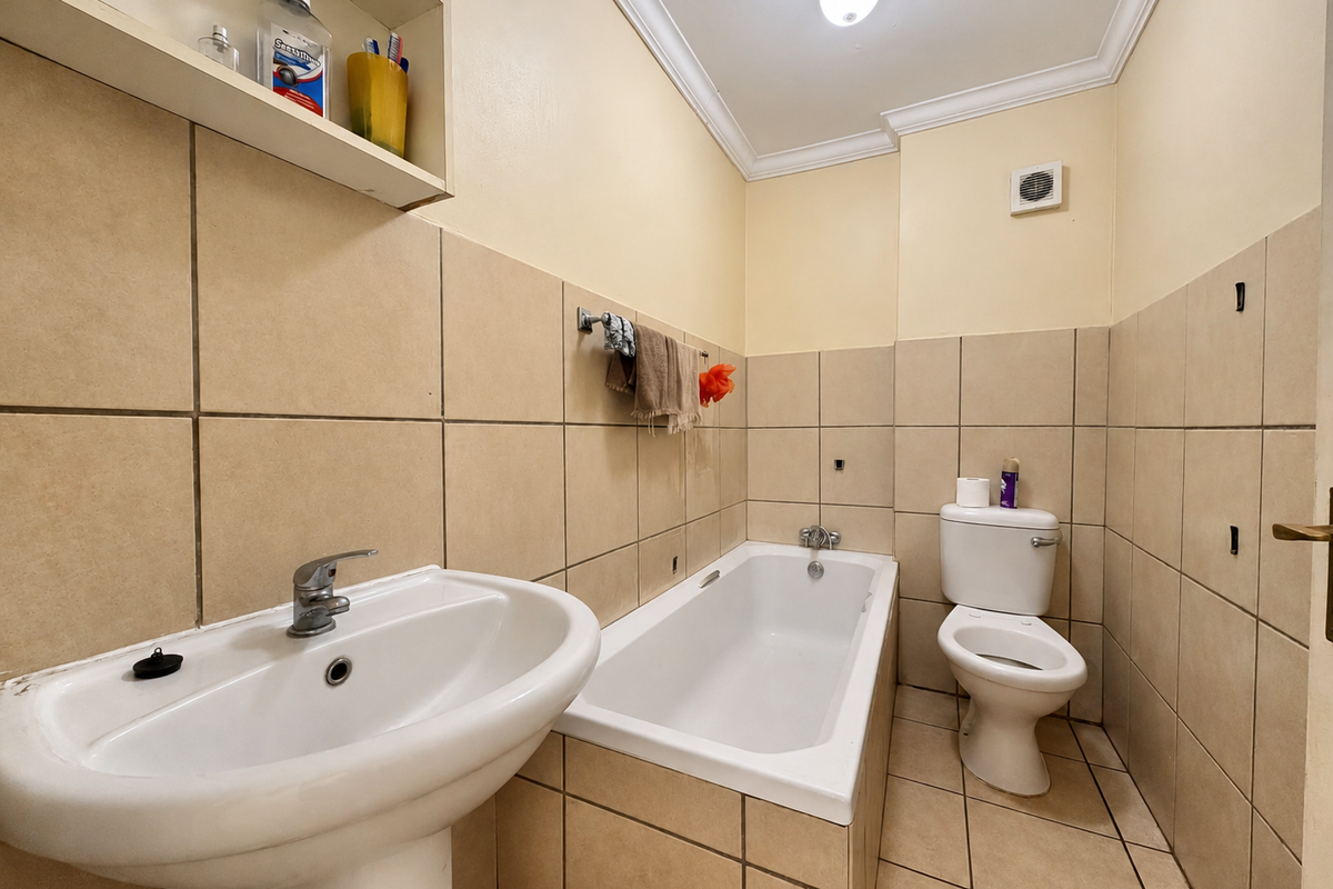 A functional bathroom featuring a pedestal basin, built-in bathtub, and toilet, finished with neutral wall and floor tiling.