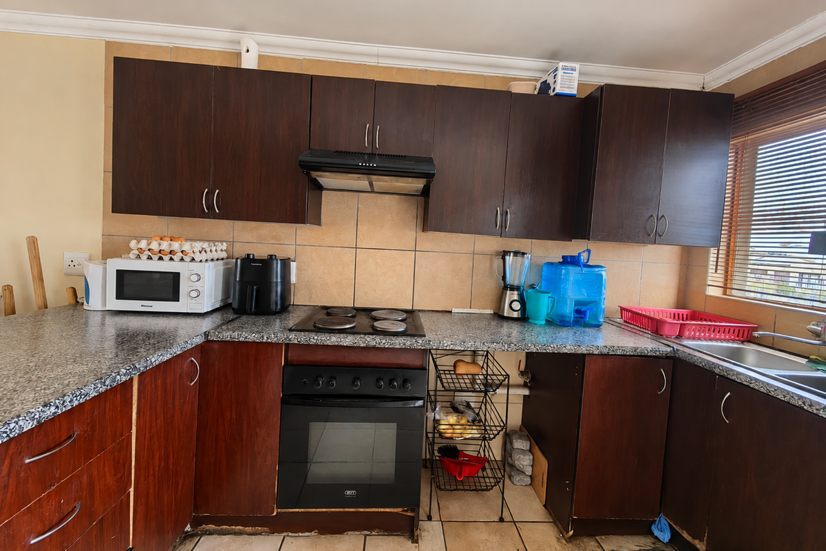 A functional kitchen featuring dark wood cabinetry, granite-look countertops, and built-in appliances, currently showing signs of wear and requiring cosmetic updates.