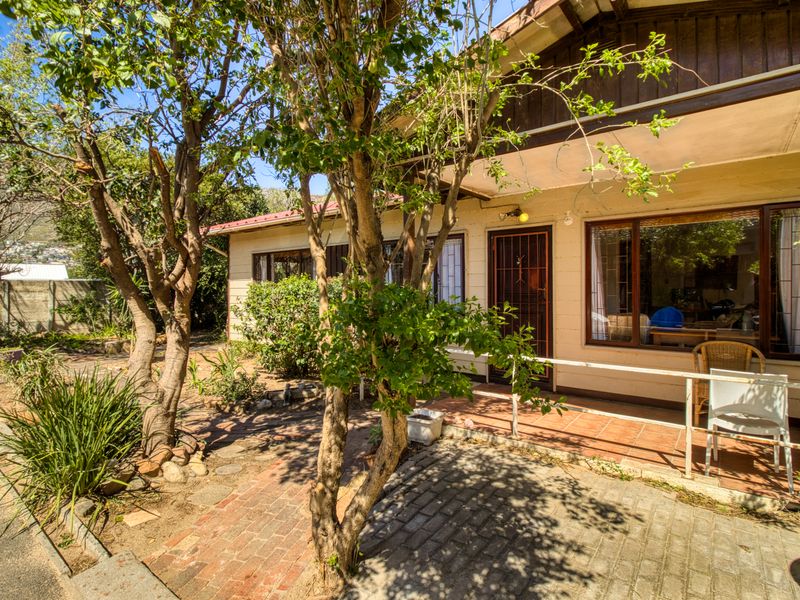 A rear exterior view of the house featuring a tiled patio, brick paved pathway, and mature garden surroundings.