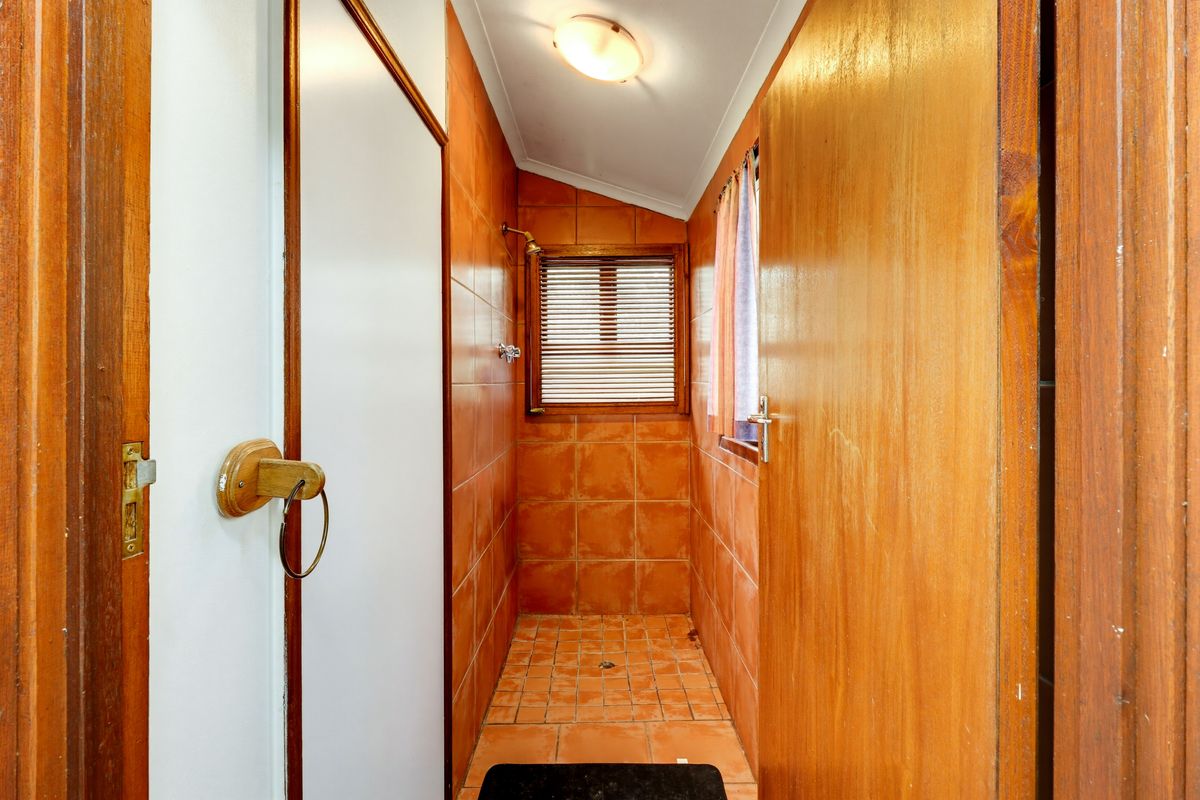 A compact bathroom featuring dated orange wall and floor tiles, a shower area, and timber door finishes.