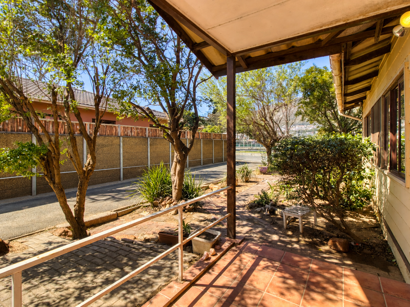 A covered outdoor patio area featuring tiled flooring and a timber roof structure, overlooking a garden space with established trees.