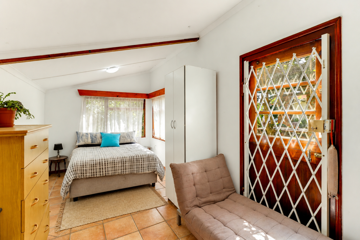 A bedroom featuring tiled flooring, exposed timber ceiling beams, and a secure exterior door with a metal security gate.