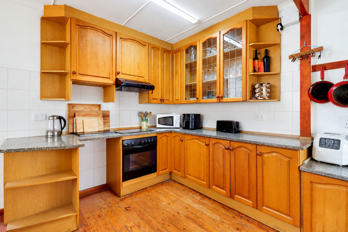 A functional kitchen featuring traditional wooden cabinetry, granite countertops, built-in oven, and hob, with a classic tiled backsplash and timber flooring.