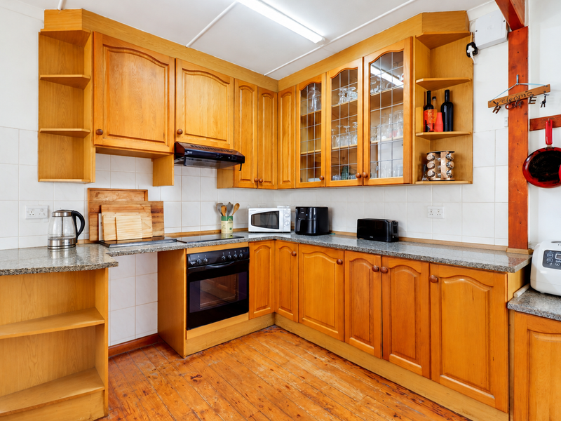 A functional kitchen featuring traditional wooden cabinetry, granite countertops, built-in oven, and hob, with a classic tiled backsplash and timber flooring.