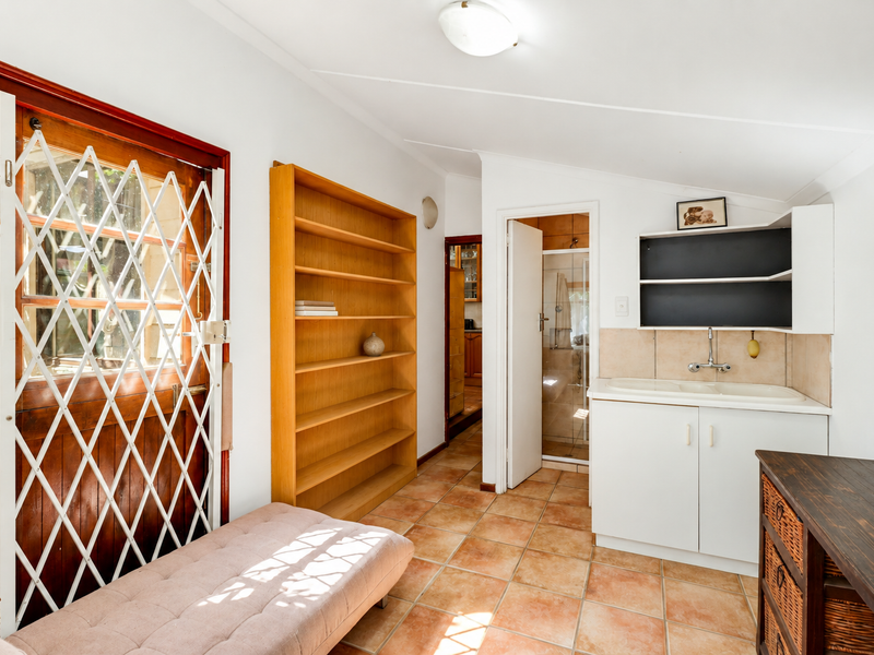 A functional utility space featuring tiled flooring, built-in cabinetry with a sink, and direct access to a secondary room and exterior via a security gate.