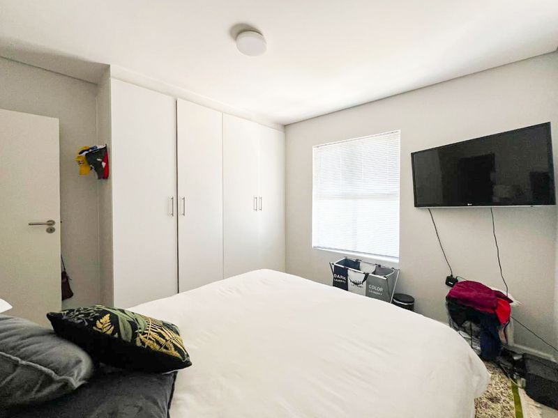 A well-lit bedroom featuring built-in cupboards, a window with venetian blinds, and neutral wall finishes.