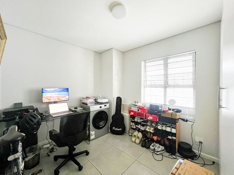 A functional office space featuring neutral tiled flooring, clean wall finishes, and a window fitted with venetian blinds, providing ample natural light.