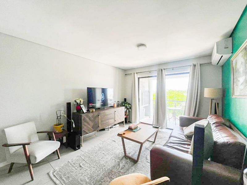 A bright living room featuring tiled flooring, a wall-mounted air conditioning unit, and direct access to a private balcony through sliding glass doors.