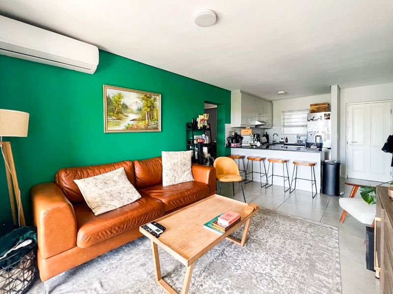 Open-plan living area featuring a kitchen with island seating and a bright green accent wall, seamlessly connected to the lounge space.