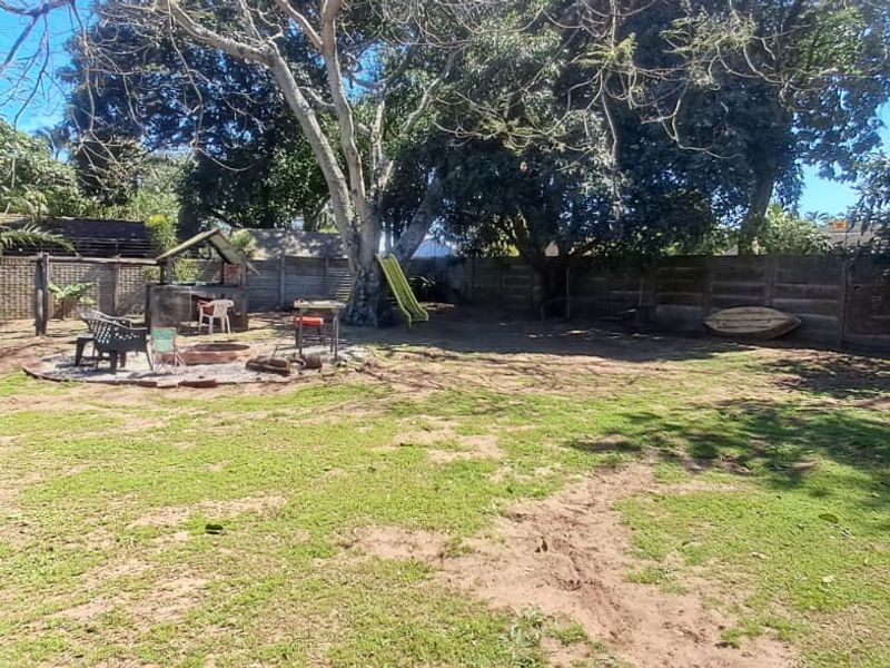 Spacious rear garden featuring a precast concrete boundary wall, mature trees, and a built-in braai area, offering significant potential for landscaping.