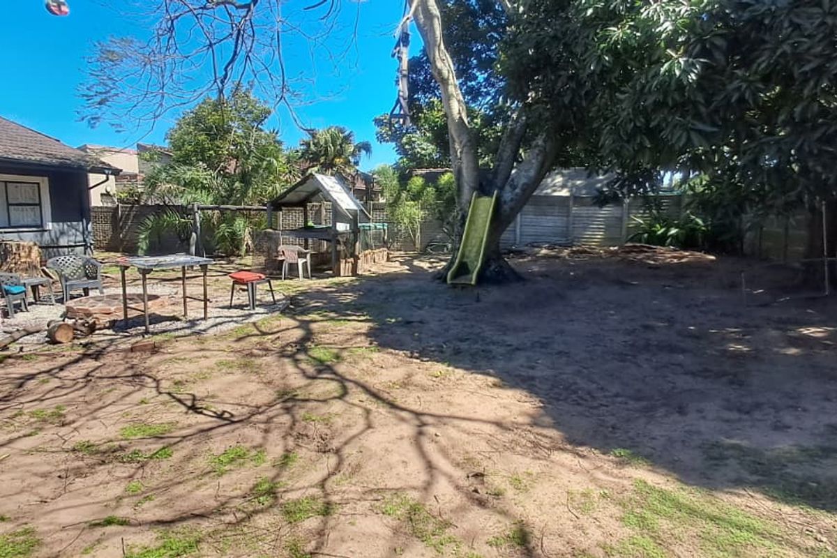 A spacious rear garden area featuring a tiled roof house extension, a concrete patio space, and established trees, offering potential for landscaping improvements.