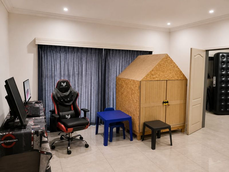 A bedroom featuring tiled flooring, recessed downlights, and a large window with curtain track, currently utilized as a multi-purpose play and study area.
