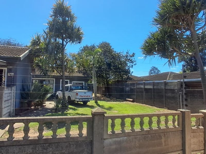 Front view of the property featuring a paved driveway, lawn area, and secure boundary wall with electric fencing.