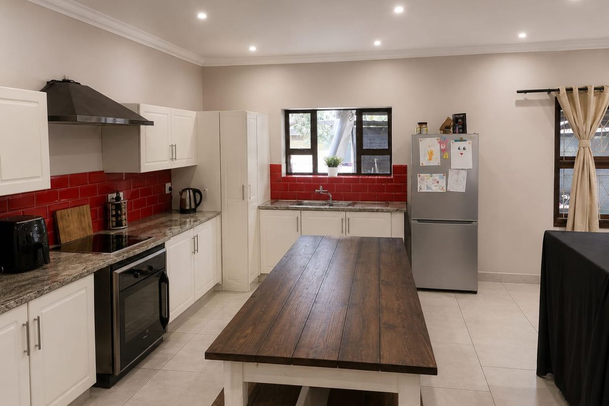 A well-maintained kitchen featuring white cabinetry, granite countertops, a red tiled backsplash, and integrated appliances, illuminated by modern recessed ceiling lights.