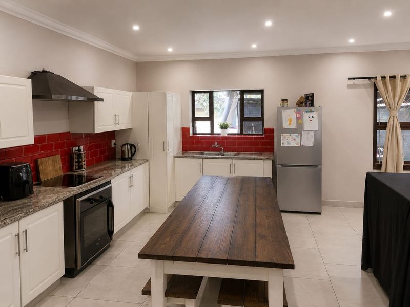 A well-maintained kitchen featuring white cabinetry, granite countertops, a red tiled backsplash, and integrated appliances, illuminated by modern recessed ceiling lights.