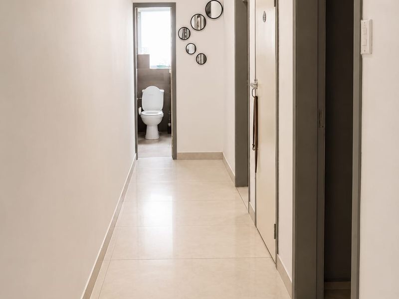 A clean, well-maintained hallway featuring neutral tiled flooring and access to adjacent rooms, including a bathroom at the end of the passage.