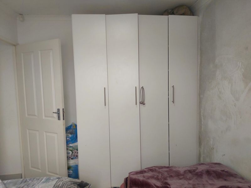 Bedroom featuring a white built-in wardrobe and a standard panel door, with visible wall surface damage requiring repair and repainting.