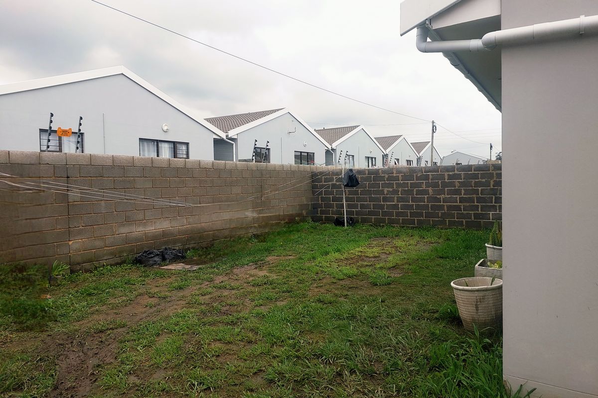 A rear garden area featuring a concrete block boundary wall with electric fencing and basic lawn space, requiring landscaping improvements.