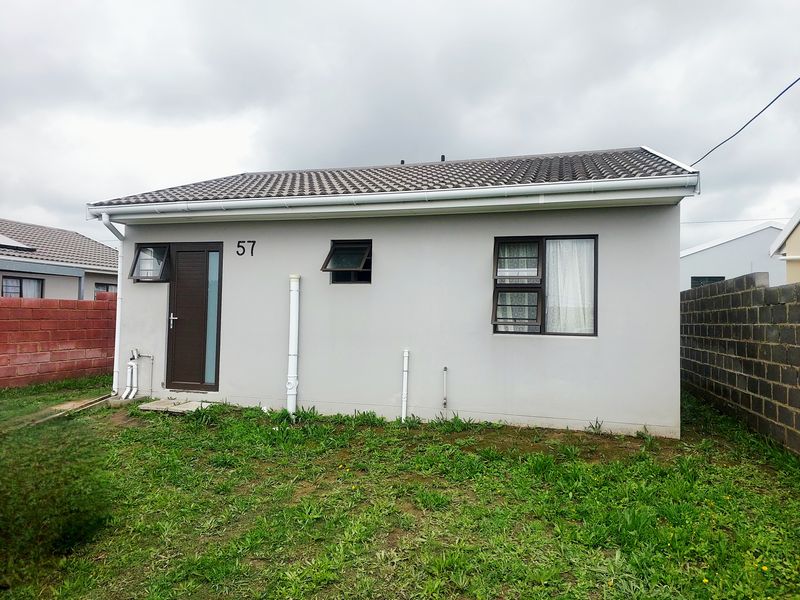 Rear view of a single-story house featuring a tiled roof, neutral exterior walls, and aluminium window frames, set against a simple grass yard.