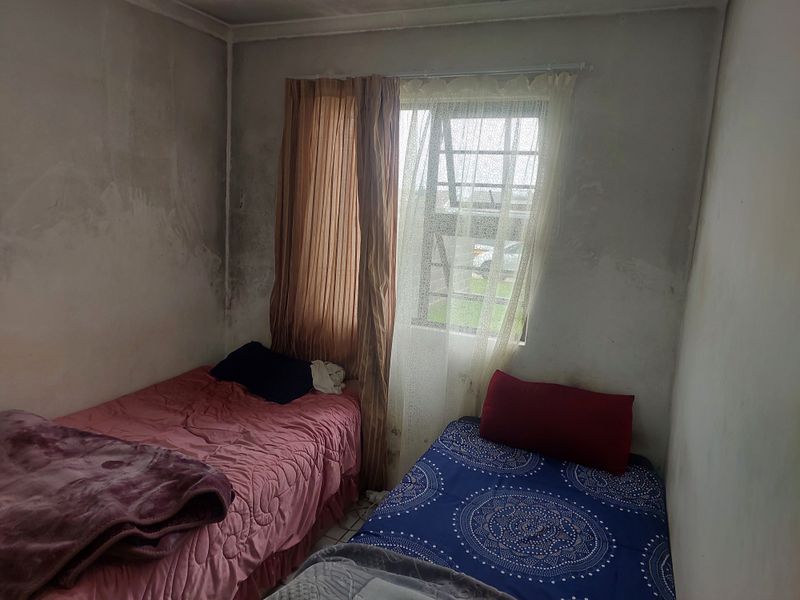 A compact bedroom featuring tiled flooring and security bars on the window, currently requiring wall surface repairs and cosmetic updates.