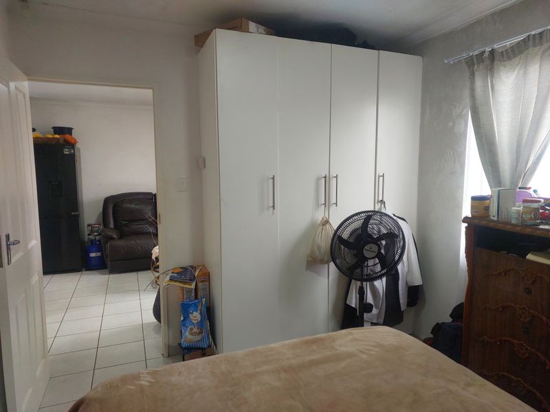 A bedroom featuring a white built-in wardrobe and a window with a curtain rail, showing signs of wear on the wall surfaces.