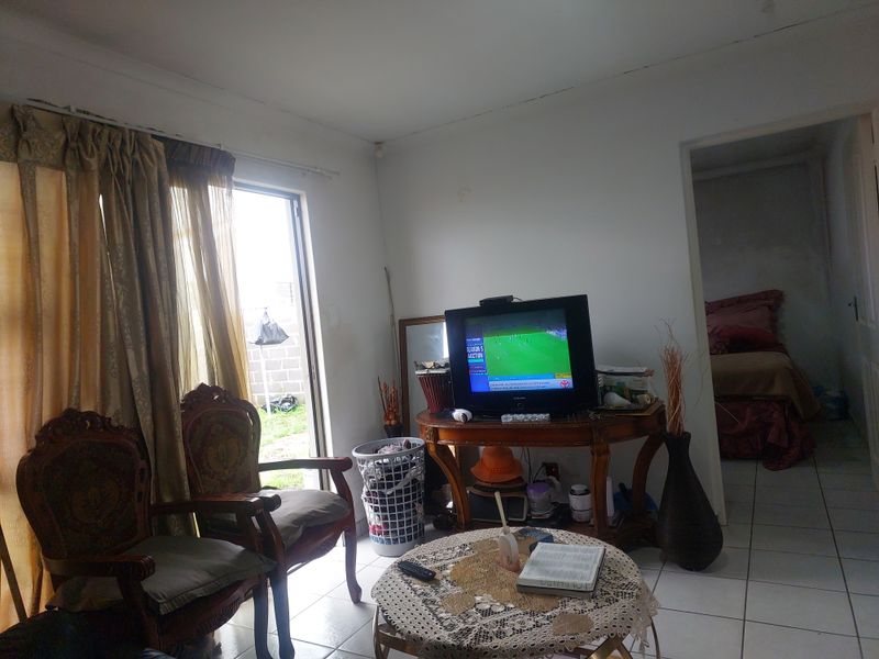 A living room area featuring tiled flooring and a sliding glass door leading to the exterior, showing signs of wear and maintenance needs.