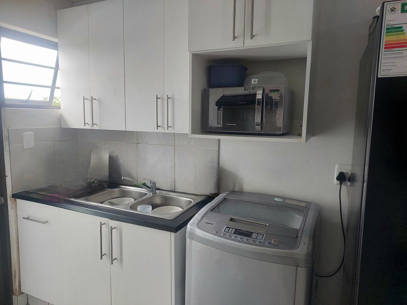 A functional laundry area featuring white built-in cabinetry, a double sink with mixer tap, and tiled splashback, providing practical utility space.