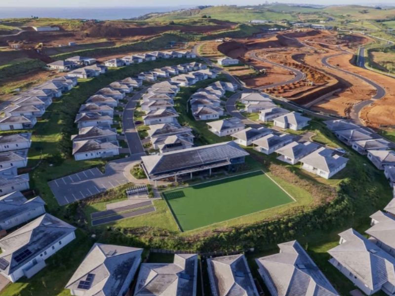Aerial view of a residential estate featuring multiple detached homes, a central clubhouse, paved infrastructure, and surrounding landscaped areas.