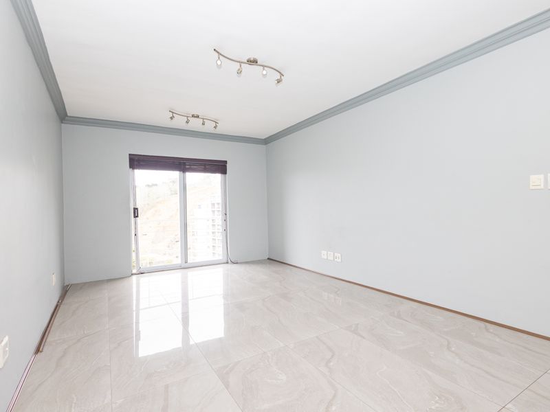 A bright, empty living room featuring polished tile flooring, crown molding, and a sliding glass door providing natural light.