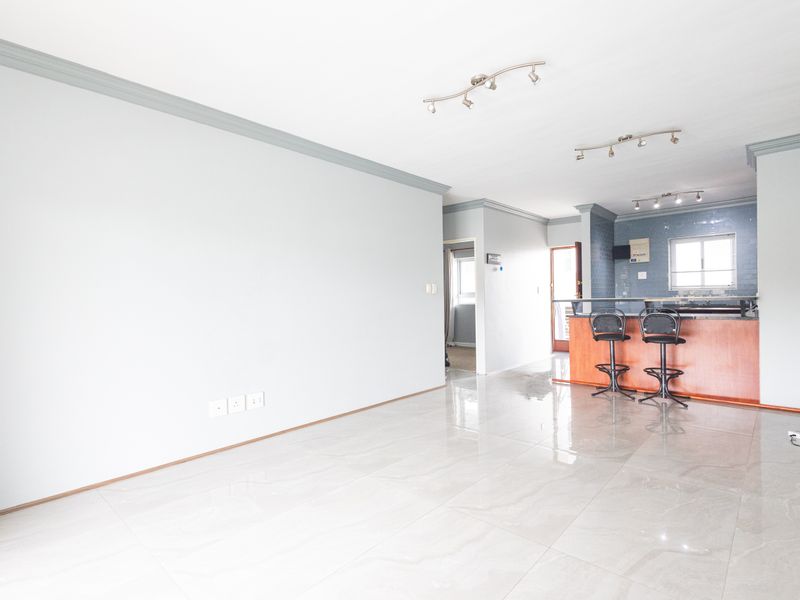 Spacious open-plan living and kitchen area featuring polished porcelain tile flooring, crown molding, and a functional breakfast bar with integrated kitchen cabinetry.