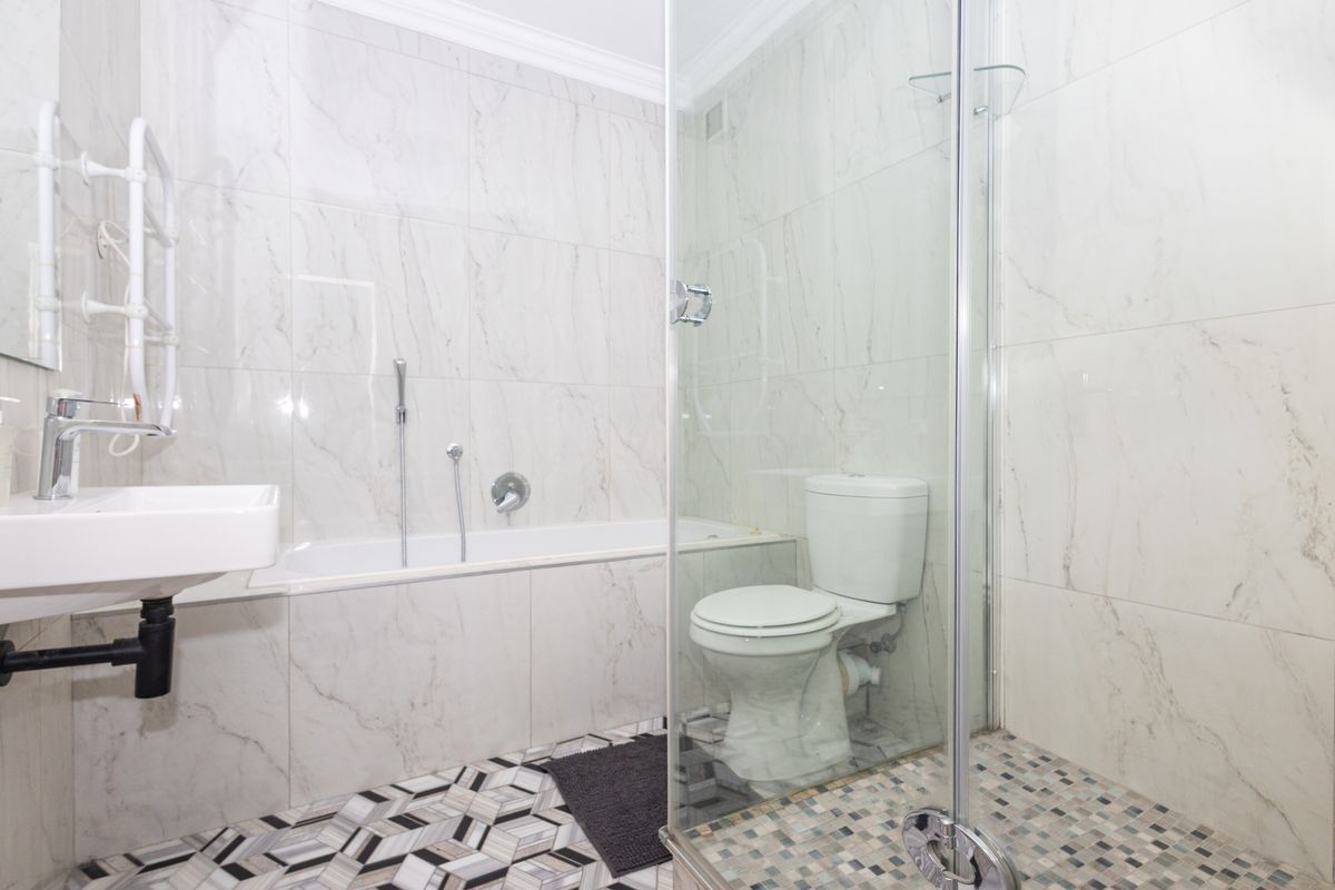 Modern bathroom featuring marble-effect wall tiling, a glass shower enclosure, a bathtub, and a wall-mounted basin with a heated towel rail.