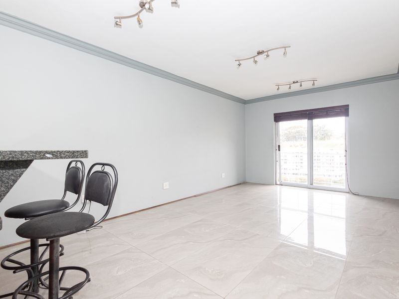 Spacious open-plan living area featuring polished tile flooring, crown molding, track lighting, and a granite breakfast bar with access to a sliding glass door.