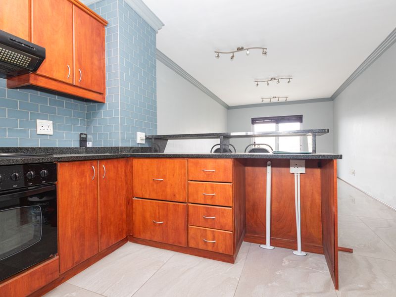 Open plan kitchen featuring wooden cabinetry, granite countertops, and a breakfast bar, flowing into an adjacent living area with tiled flooring.
