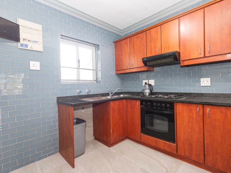 A functional kitchen featuring wooden cabinetry, granite countertops, a built-in oven with hob, and a blue subway tile backsplash.