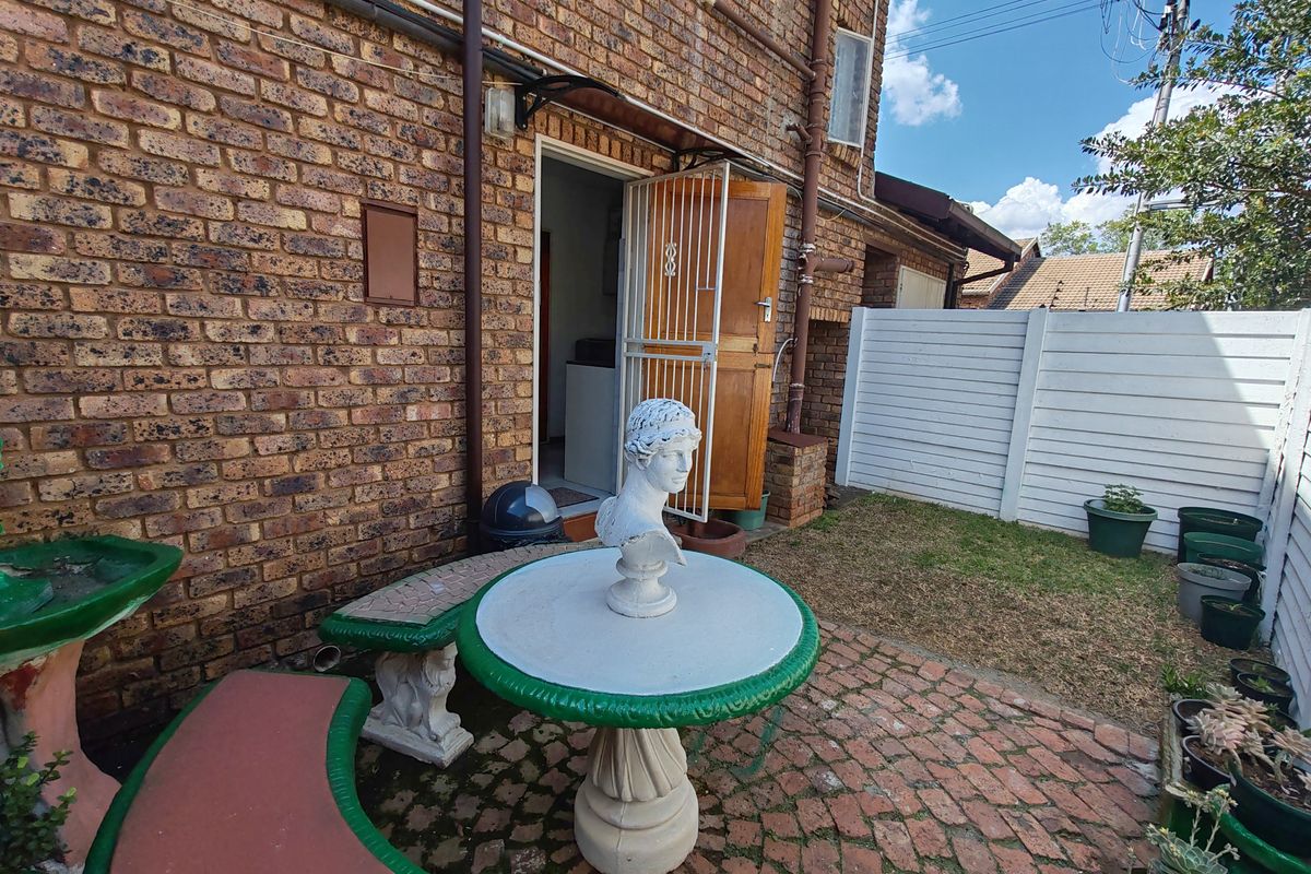 A rear exterior view of the townhouse featuring a face brick facade, a paved patio area, and a white boundary fence.