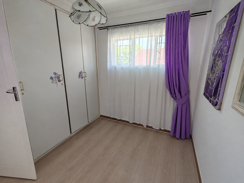 A bright, empty bedroom featuring light-toned laminate flooring and ample built-in cupboard storage space.